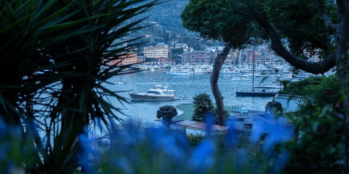 People relaxing by a marina with luxury yachts and modern waterfront buildings in the background.
